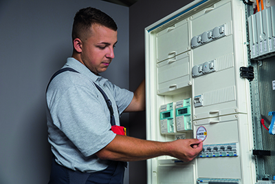 ELektriker klebt E-CHECK Plakette an Verteiler